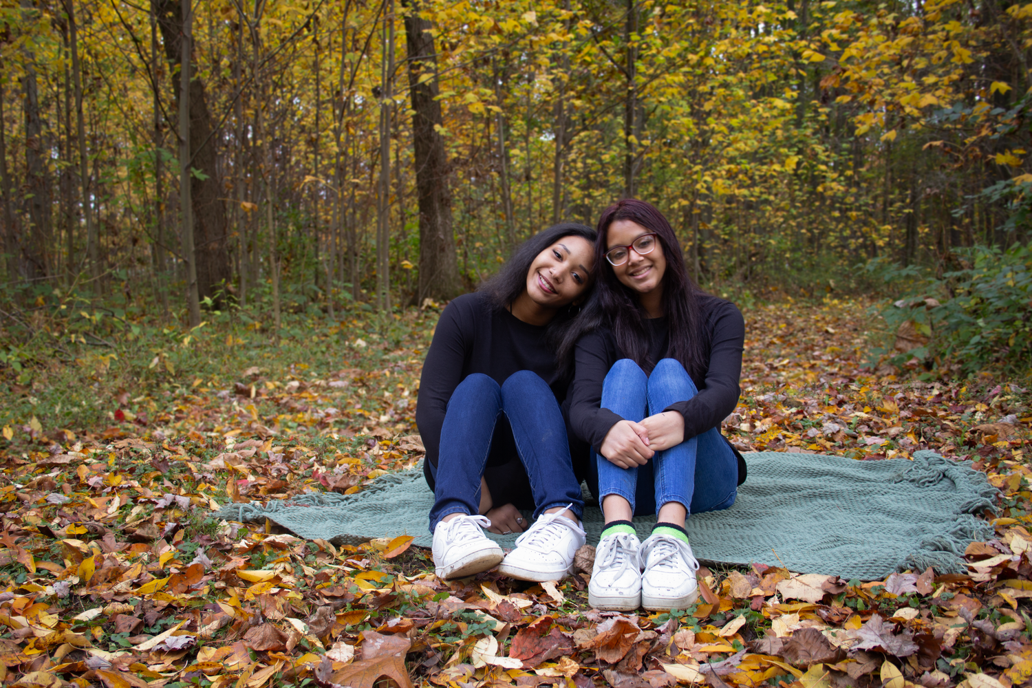 Two people sitting on a blanket surrounded by autumn leaves in the forest.