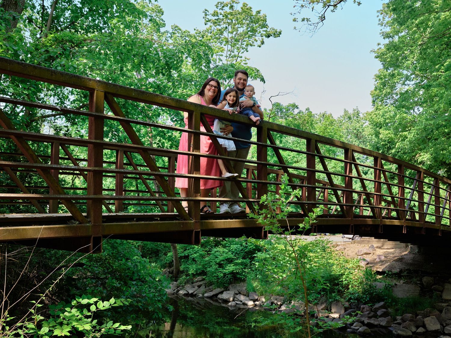 Group of people observing nature from wooden bridge walkway in lush green forest surroundings.