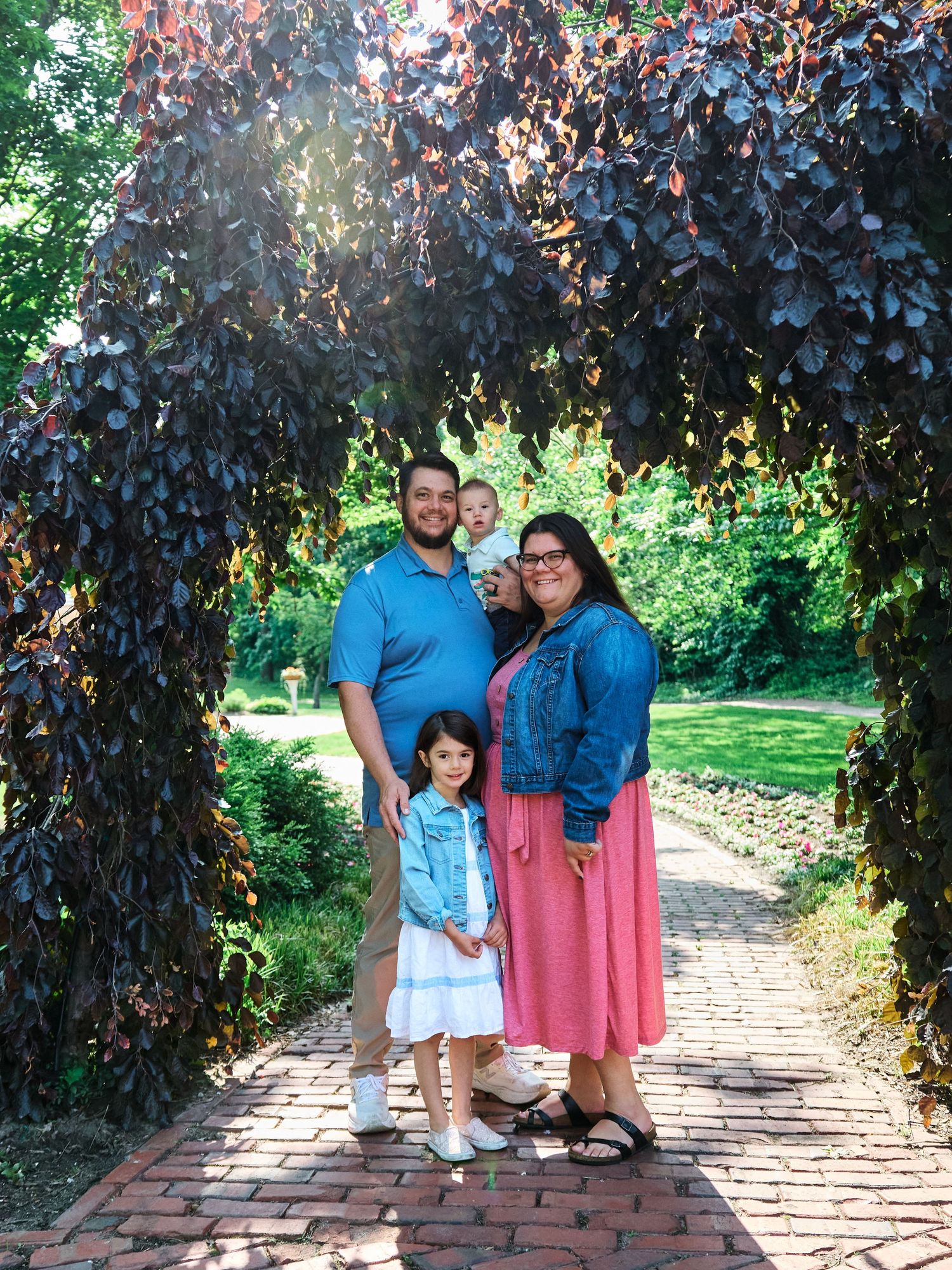 Candid family photo series of three people walking and posing together on a brick path surrounded by lush purple foliage.