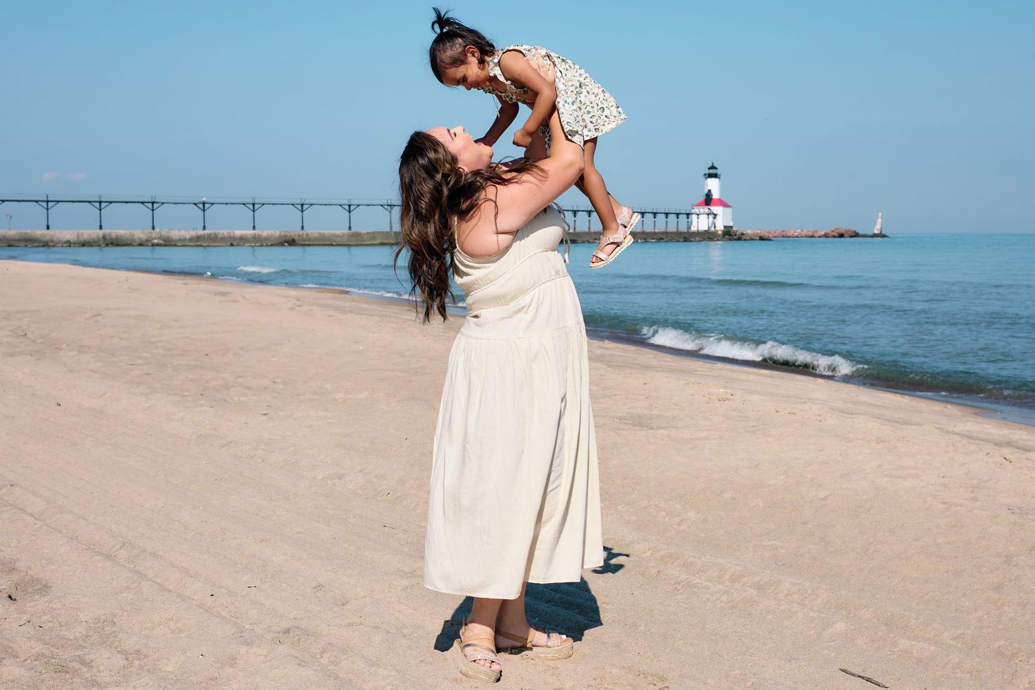 A joyful moment shared between two people on a sandy beach with a lighthouse in the distance.