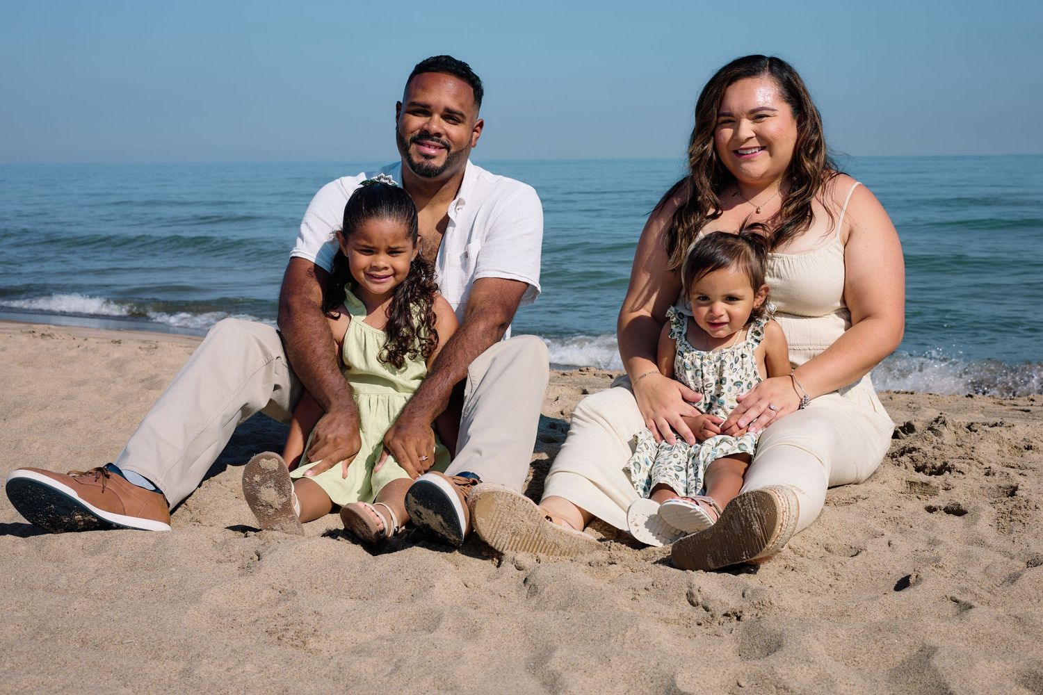A family sits together on sandy beach with ocean waves in the background.