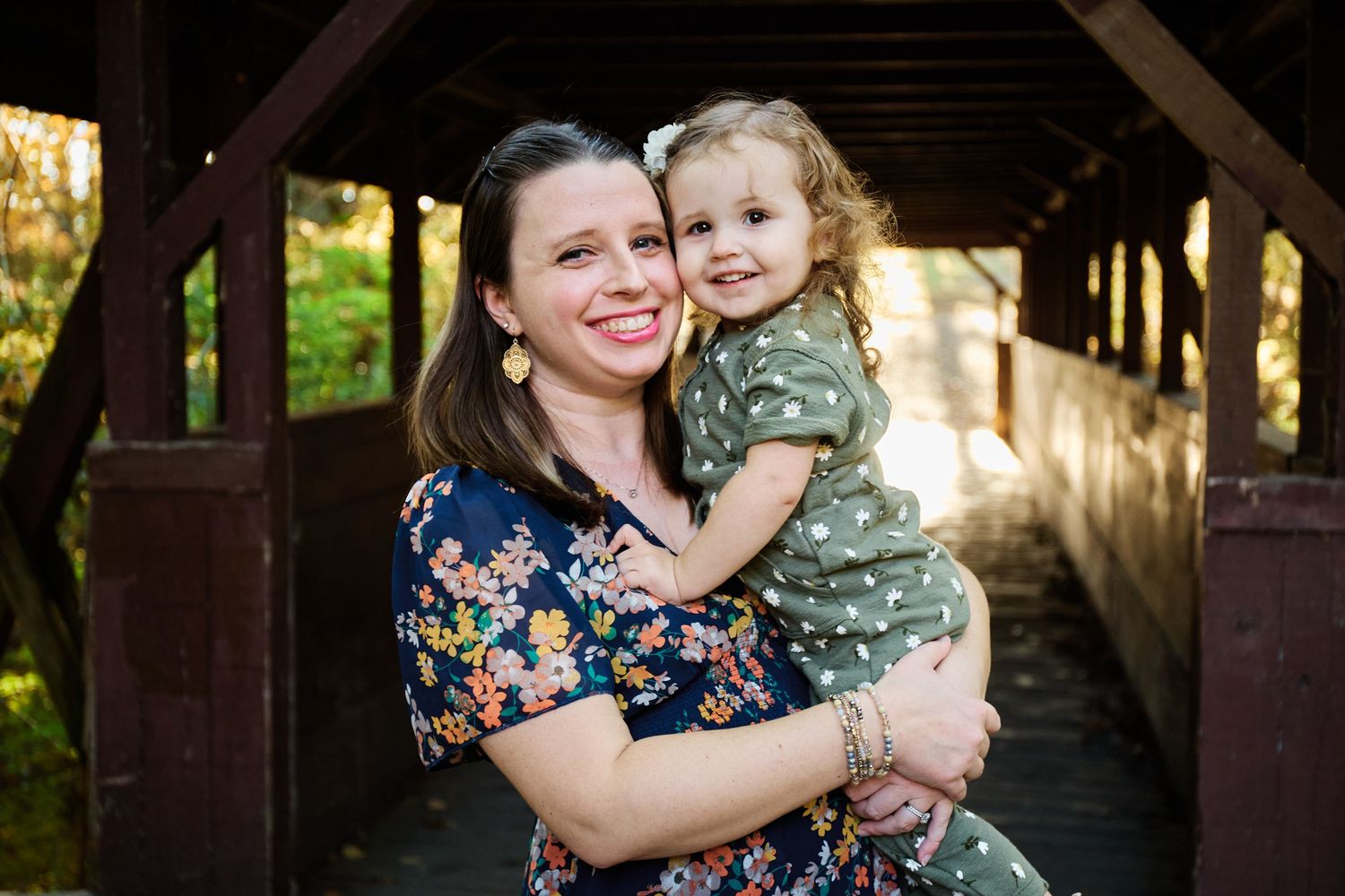 Tender moment between parent and child at covered wooden bridge during family photo session.