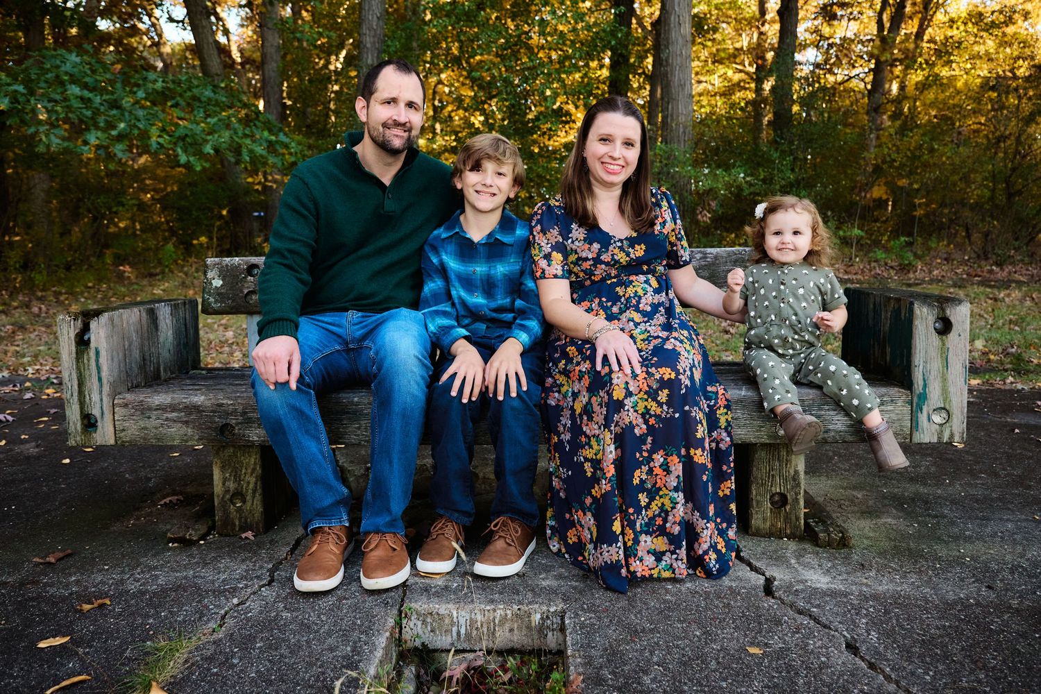 Family of four sitting together on stone bench in outdoor autumn setting.