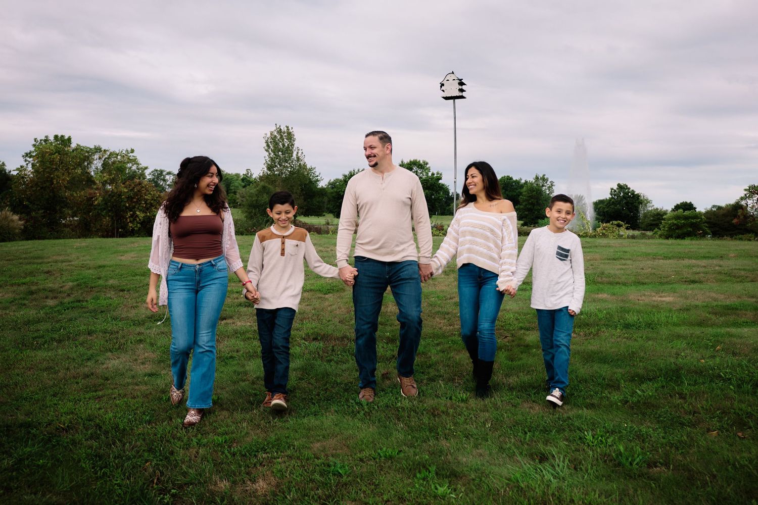 Family walking together across a green field under cloudy skies.