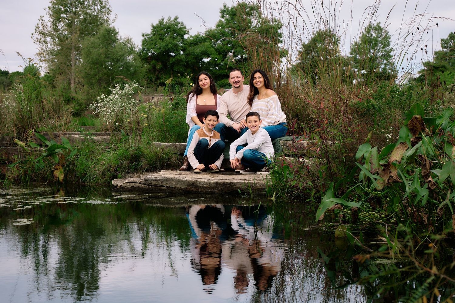 Group portrait by a pond with reflections in the water and natural greenery surrounding.