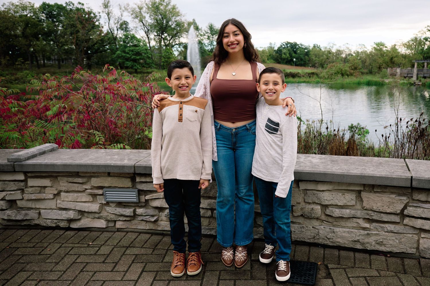 Three people standing together against a stone wall with colorful flowers and a lake in the background.