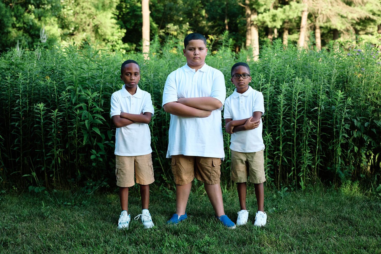 Three people in white shirts standing against a green summer background.