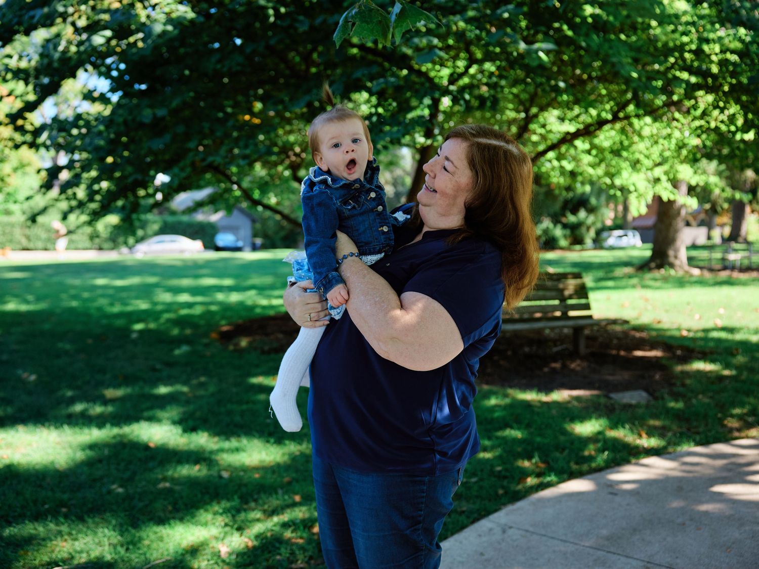 Two people embrace joyfully in a lush green park setting during a sunny summer day.