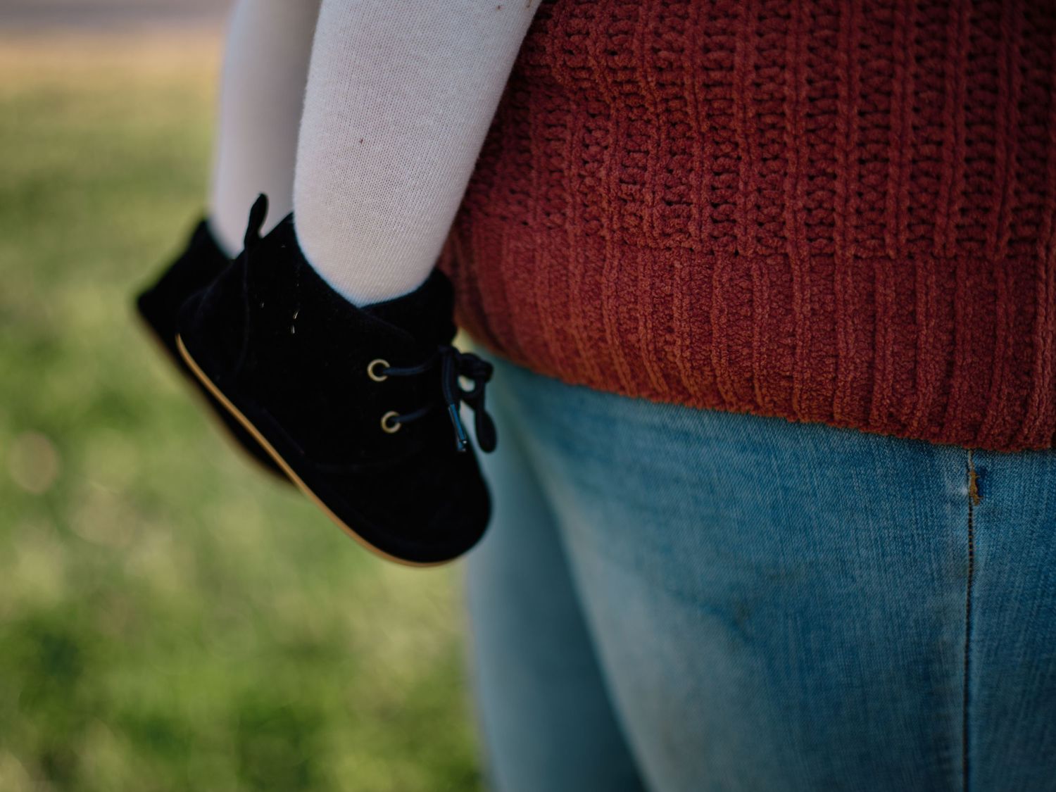 Close-up detail of a black shoe against red knit sweater and blue jeans.