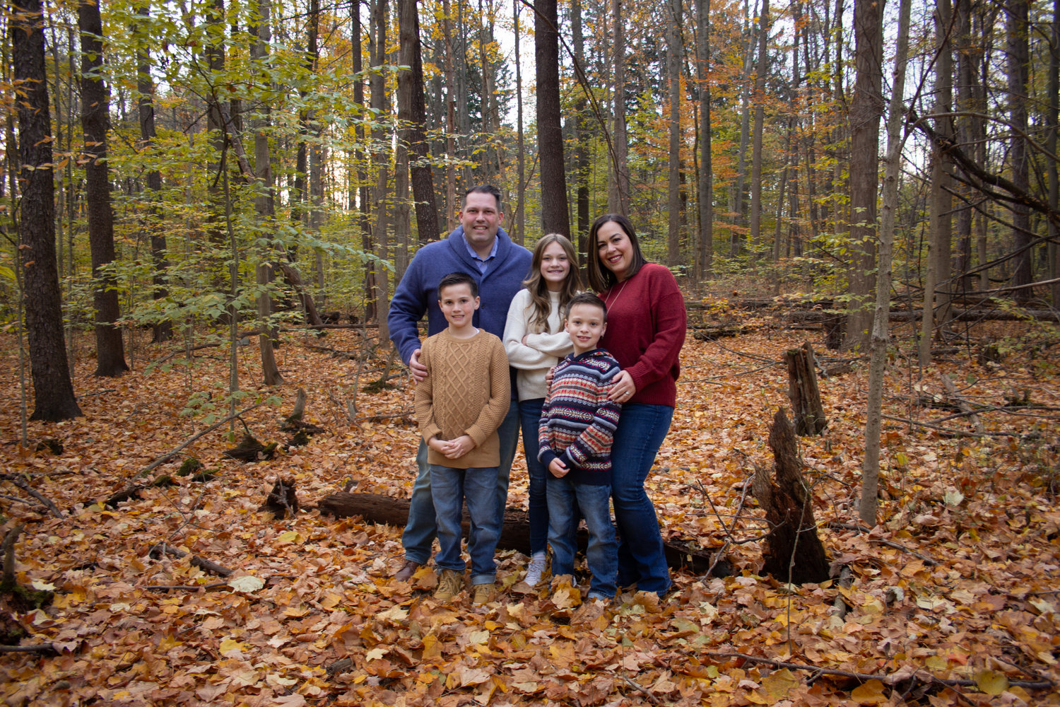 Family photo session in a colorful autumn forest with fallen leaves.