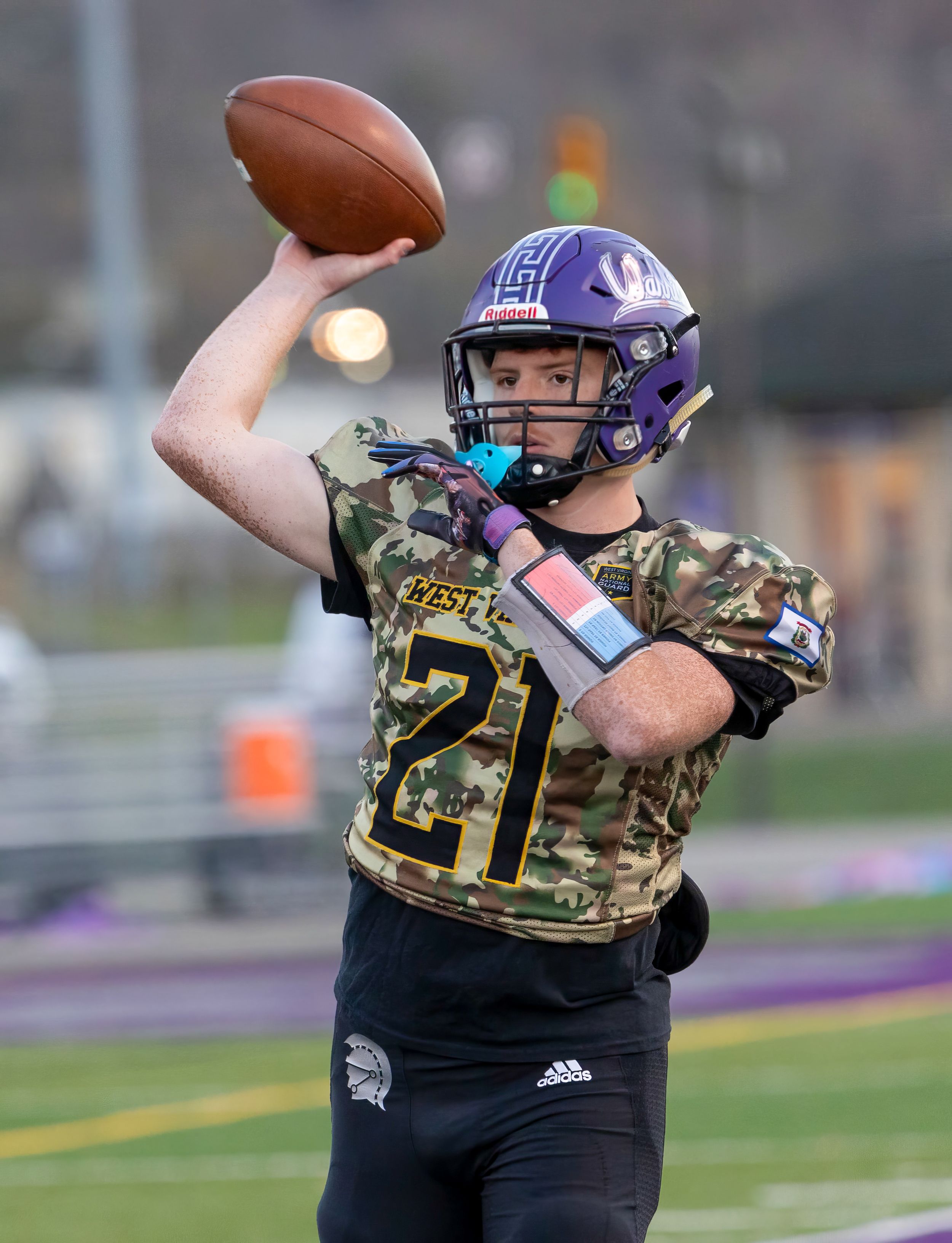 Football player in camo jersey prepares to throw pass during game.