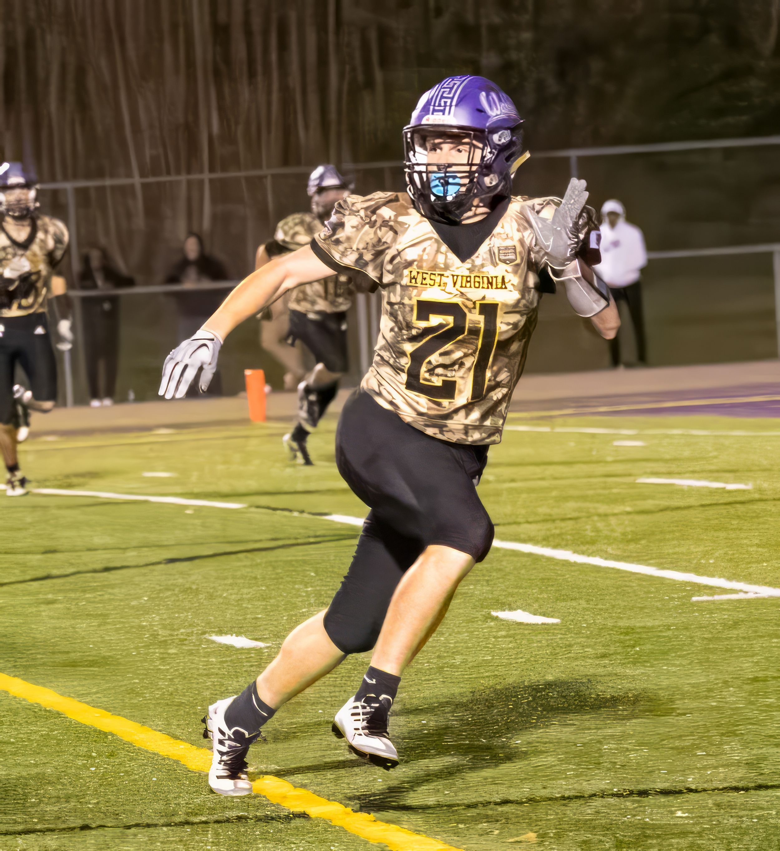 Football player in camo jersey number 21 runs on field during night game.
