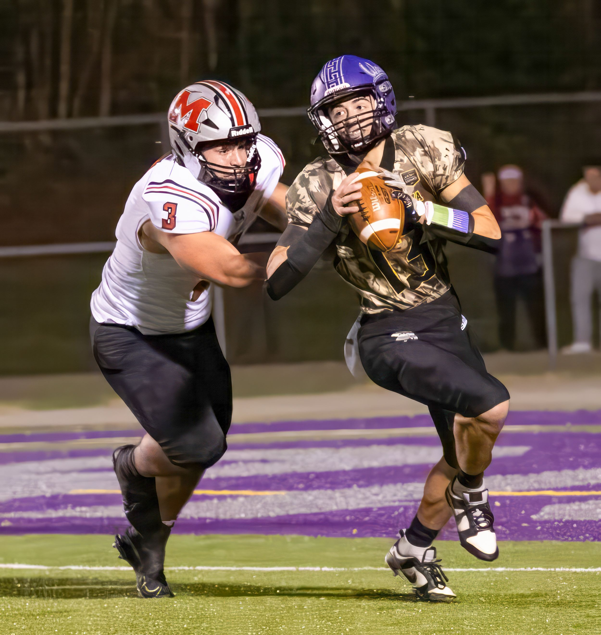 Football players collide during intense tackle attempt on purple field.