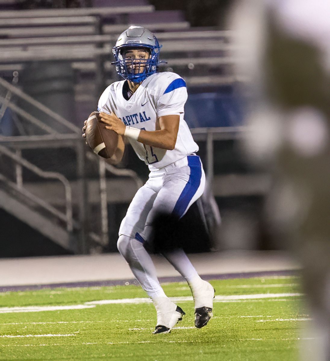 Football player in white and blue uniform prepares to throw ball during nighttime game.