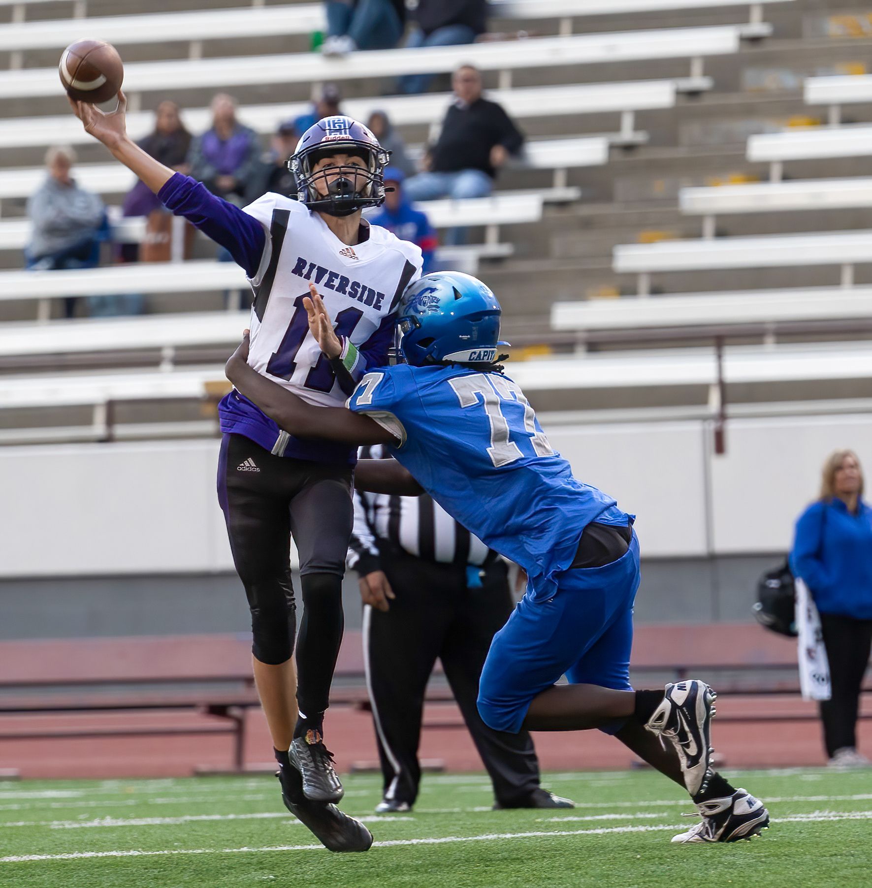 Quarterback throws ball while defender attempts tackle during football game.