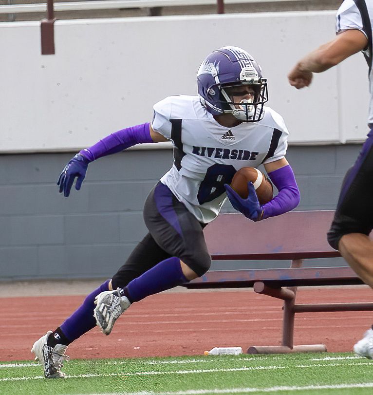 Football player in purple and white uniform carries ball while running during game.