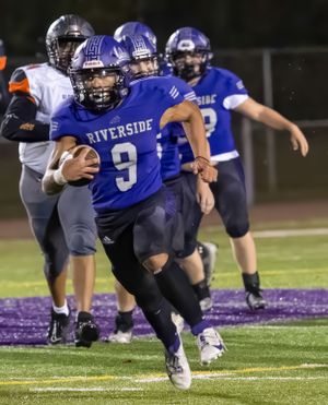 Riverside quarterback in blue uniform carries ball during football game.