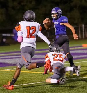 Football player jumps over defender while opposing team members pursue during game.