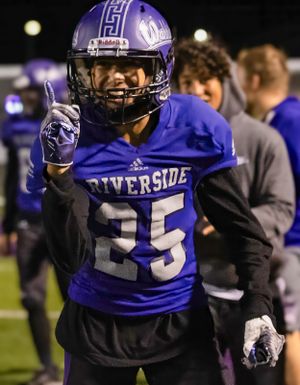Riverside football player in purple jersey signals during night game.