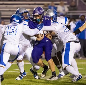 High school football players in purple and white uniforms collide during a defensive tackle on the field.