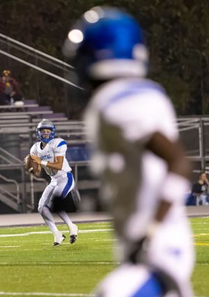 Football player in white uniform drops back to pass while teammate blocks in foreground.