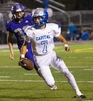 Football player in white uniform carrying ball runs past defender in purple during game action.