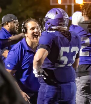Football coaches and players celebrate on sideline during game wearing purple uniforms.