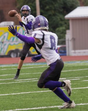 Football players in purple uniforms practice passing drills during team practice.