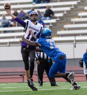 Football player throws pass while being pressured by defender during game action.