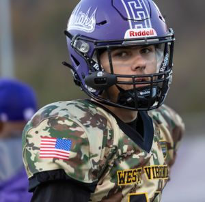 Football player wearing purple helmet and camouflage uniform with American flag patch.