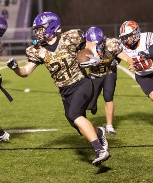 Player in camouflage jersey number 21 runs with ball during nighttime football game.