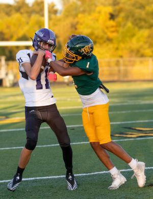 Two football players clash during play, one in white jersey and one in green and gold uniform.