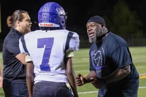 Coaches talk with player during football game sideline discussion.