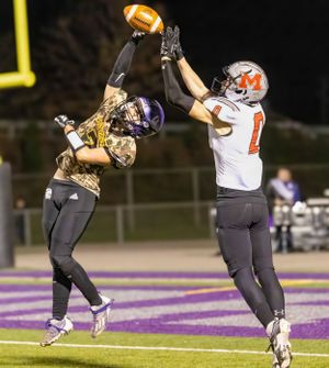 Two football players leap high to compete for a pass during a nighttime game on a purple field.