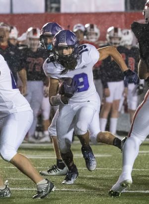 Running back carries football through snowy conditions in white and purple uniform.
