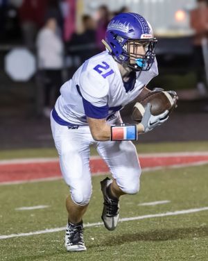 Football player in white uniform carries ball during night game action.
