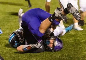 Football player in purple uniform falls to ground during game action.