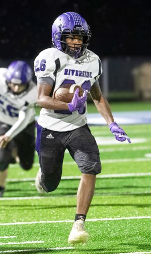 Football player in purple and white Riverside uniform runs with ball during nighttime game.