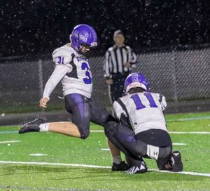 Riverside football players attempt field goal kick during snowy night game.