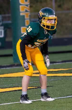 Football player in green and gold uniform crouches in ready position on artificial turf field.