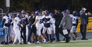 Football players and coaches gather on the sideline during a nighttime game.
