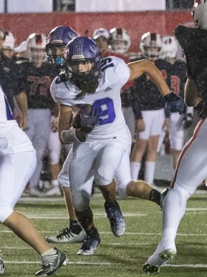 Action shot of a football player in purple and white uniform carrying the ball during a game.