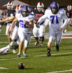 Football players chase after a loose ball on the field during competitive play.