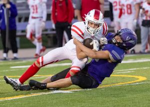Red and white uniformed player tackles opponent in purple during football game.