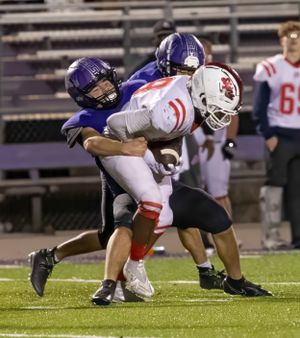 Purple uniformed defender tackles opponent in white and red during nighttime football game.