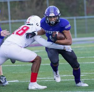Football action shot shows purple and white uniformed players in contact during a tackle.