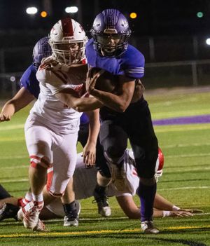 Players from opposing teams clash during nighttime football game on artificial turf.