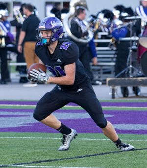 Football player in black and purple uniform runs with the ball during a game.