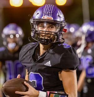 Football player in black uniform and helmet holds ball under stadium lights.
