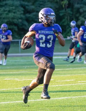 Running back in blue Riverside jersey carries the ball during a football game.